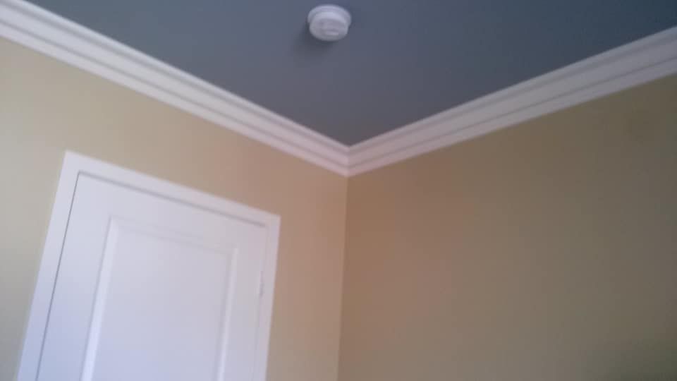 Corner of a room with blue ceiling, beige walls, white crown molding, and a white door.
