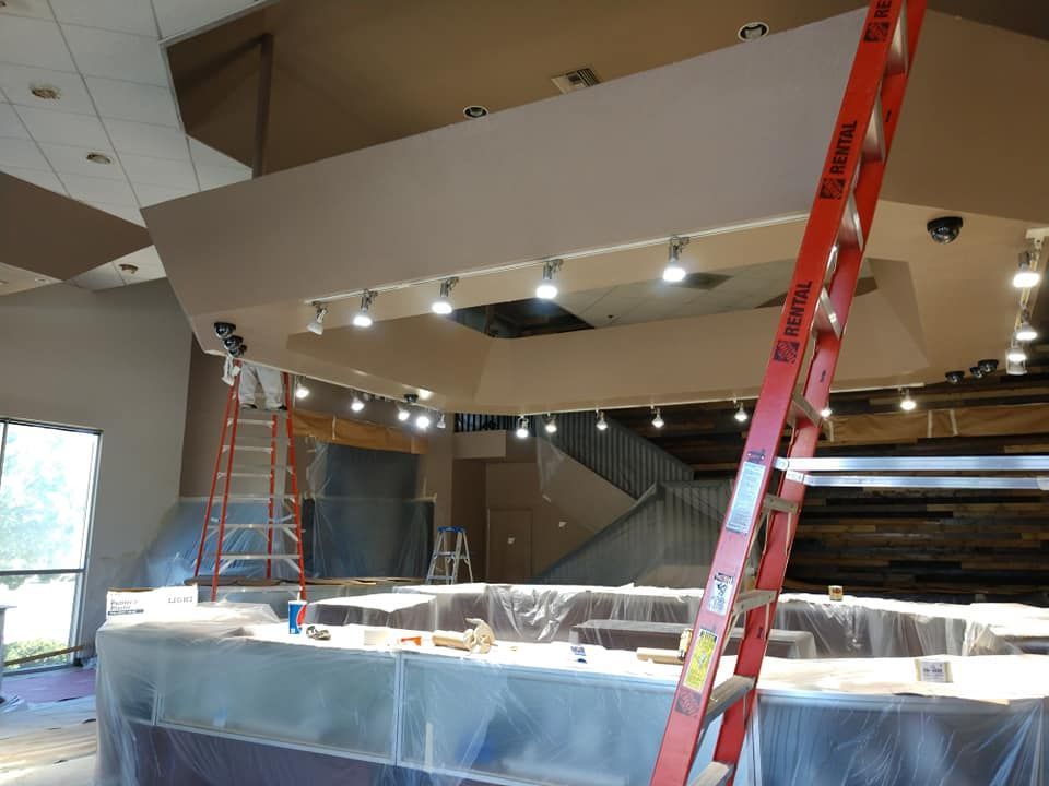 Interior renovation with a ladder, new lights, covered bar, and unfinished walls.