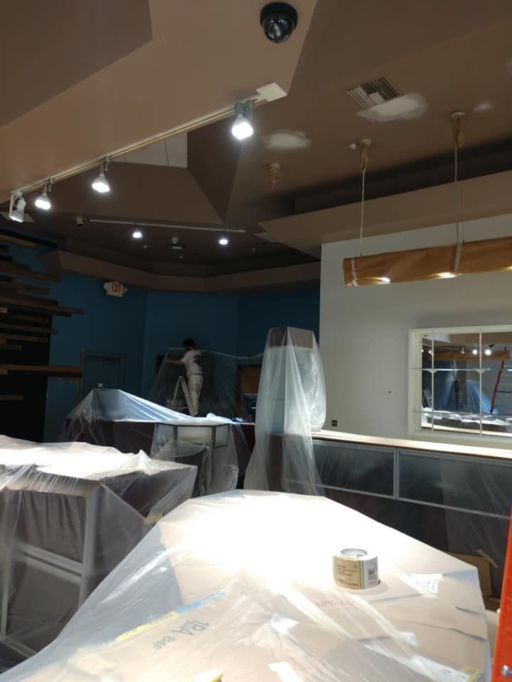 Restaurant interior under construction; covered tables and person paining wall. Brown ceiling and blue wall.