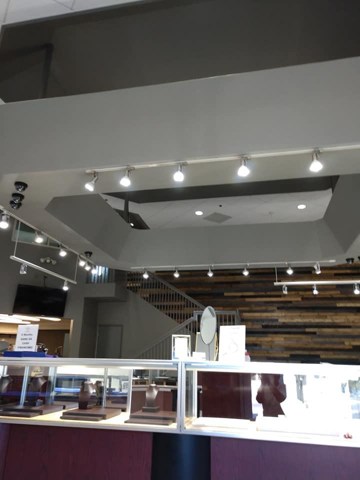 Jewelry store interior: display cases, lights, wood wall, staircase, and overhead lighting.