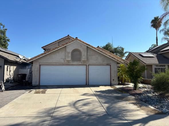 Two-car garage with white doors on a sunny day. Concrete driveway; neighboring houses visible.