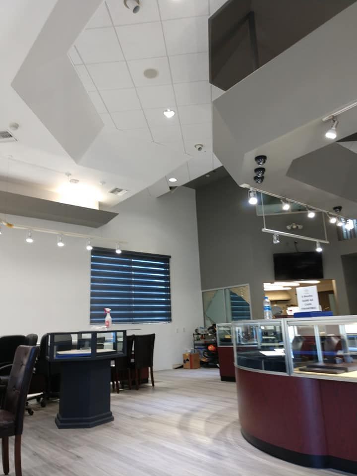 Jewelry store interior with display cases, seating, and high ceilings. Blue blinds, gray and white walls.