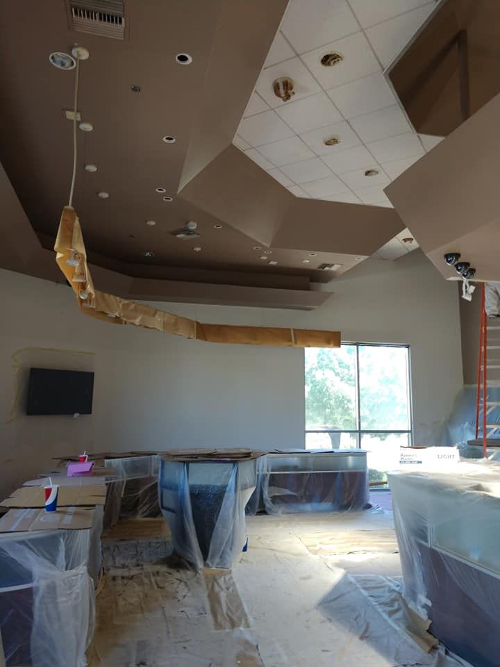Interior of a room under renovation; tan ceiling with interesting angles, unfinished wood strip hangs down, counters covered in plastic.