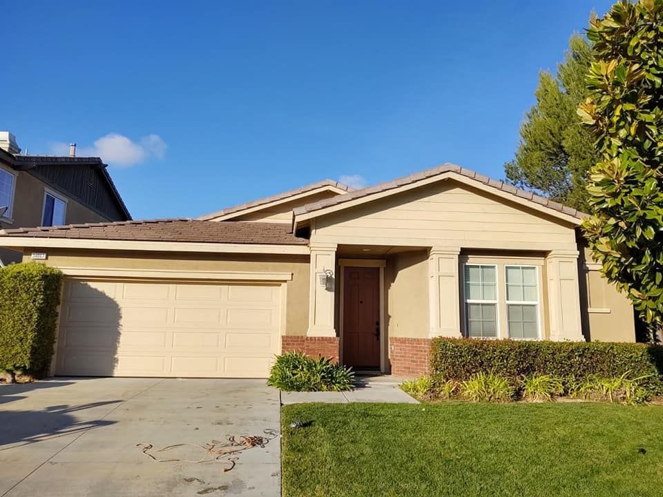 Beige house with brown roof, garage door, green lawn, and blue sky.