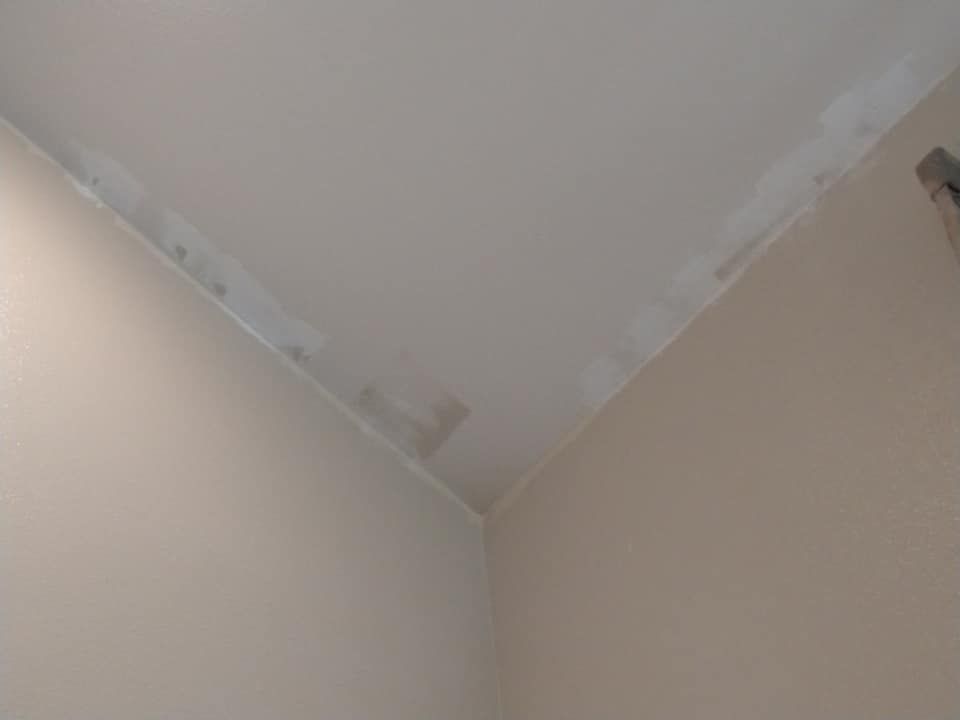 Off-white ceiling meeting beige walls at a corner, showing patches of drywall compound along the edges.