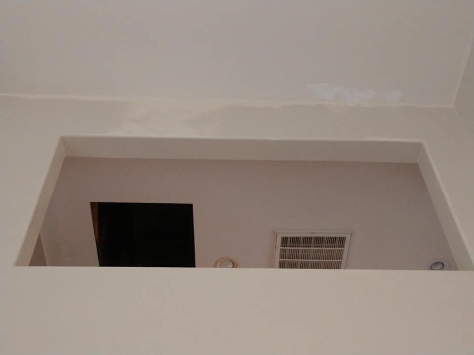 Interior view of a wall with a rectangular opening, a dark hole, and a barred window.