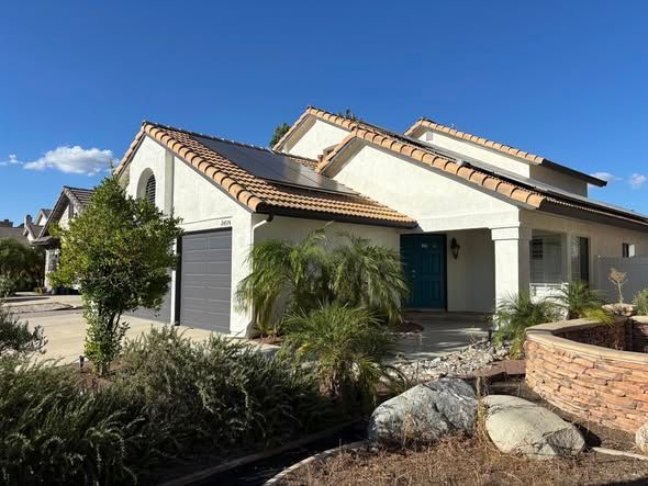 House with solar panels on roof, teal front door, gray garage door, and landscaping.