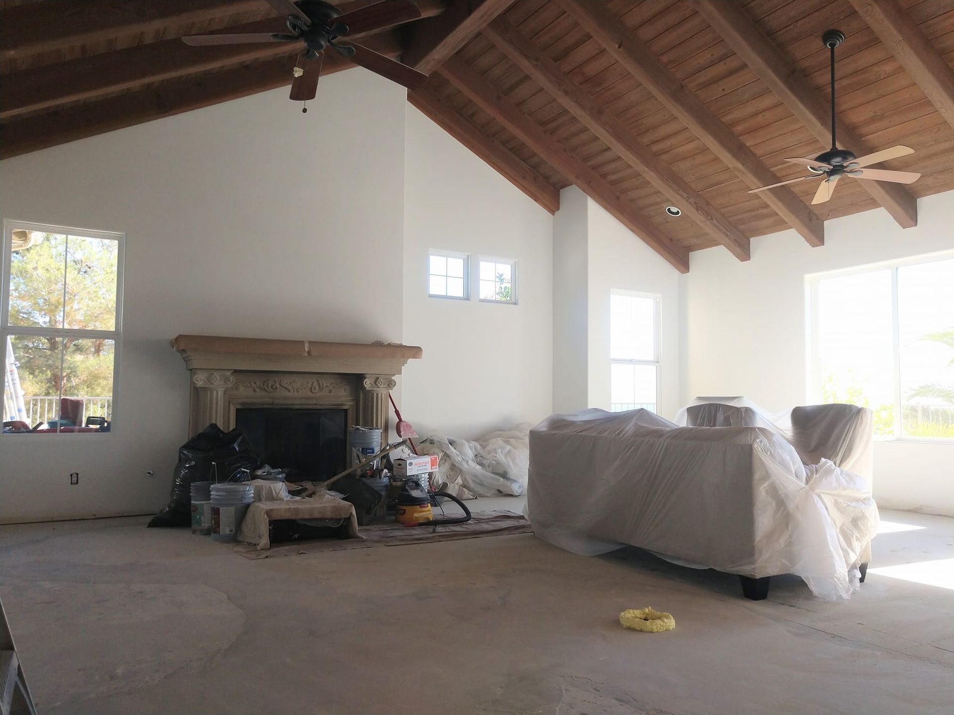 Spacious room under renovation with a fireplace, covered furniture, and exposed wooden beams.