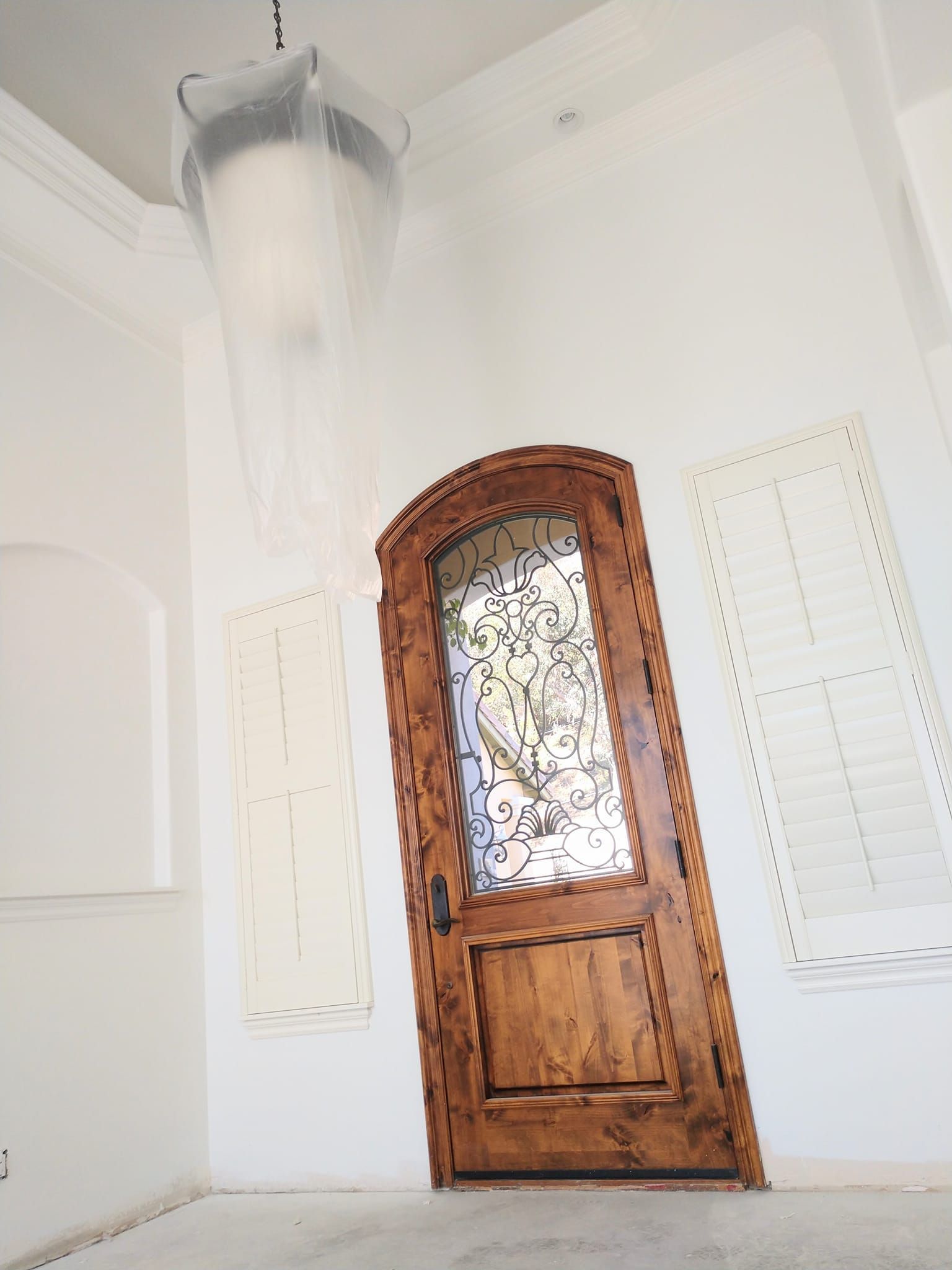 Wooden front door with glass panel and white walls, light fixture covered in plastic.