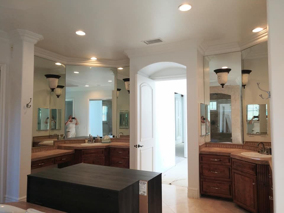Bathroom with dark wood cabinets, large mirrors, and an island. A person is reflected in the mirror.