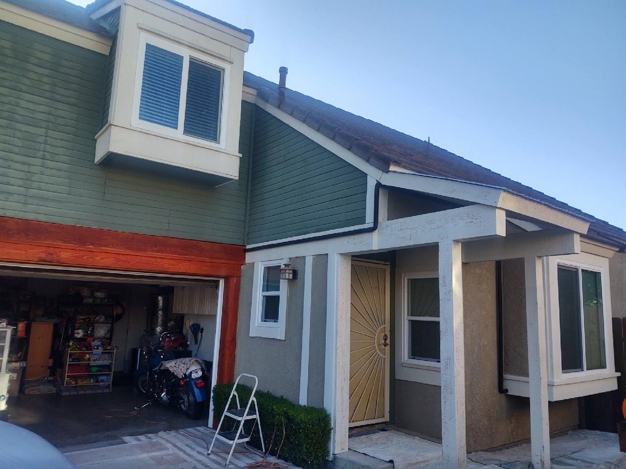 A house exterior with a garage, porch, and green siding. A motorcycle sits in the garage.