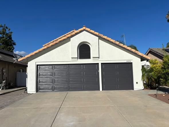 Garage with three dark gray doors, white walls, arched vent, and terracotta roof against blue sky.