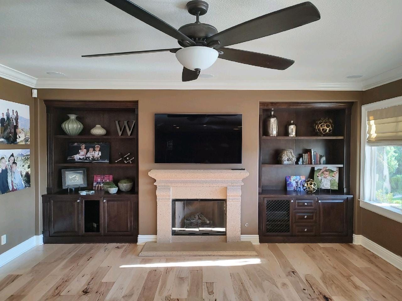 Living room with built-in shelves, fireplace, and TV, brown tones, hardwood floor, and ceiling fan.