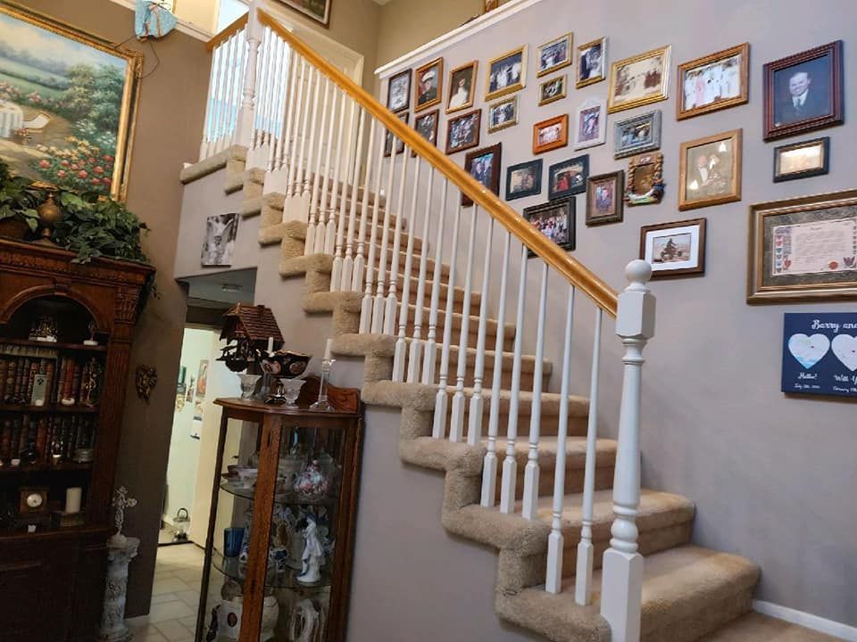 A staircase in a home with carpeted steps, a gallery wall of framed photos, and a tall wooden curio cabinet.