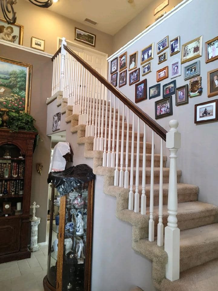 Staircase ascending with beige carpet, white spindles, and brown handrail. Photos adorn the wall.