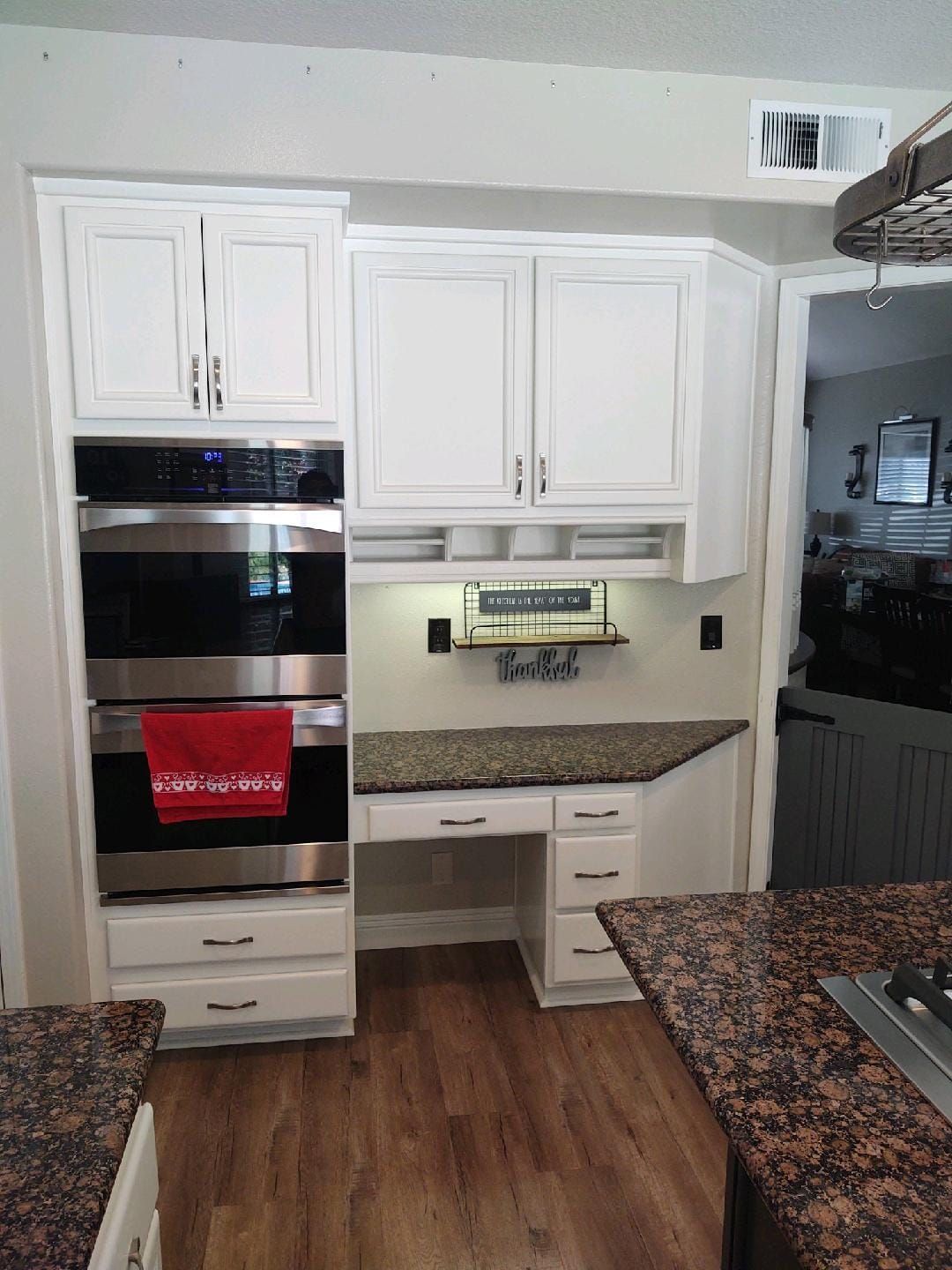 White kitchen cabinets with built-in oven, desk with granite countertop, and wood floor.