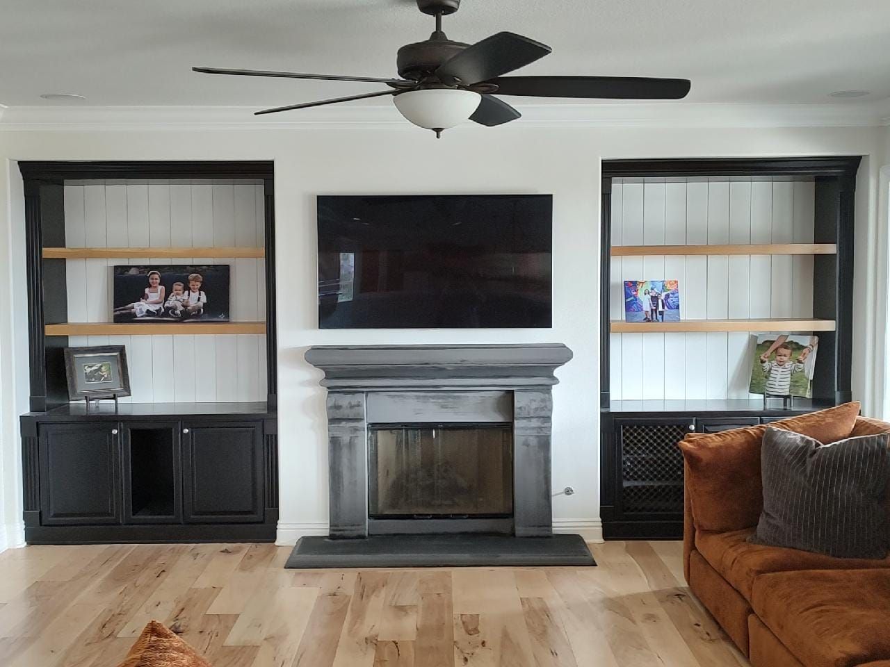 Living room with fireplace, TV, and built-in black bookshelves on each side with wooden shelves.