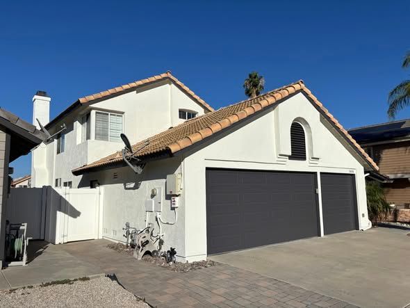 Two-story house with a white exterior, gray garage doors, and a tile roof against a clear blue sky.