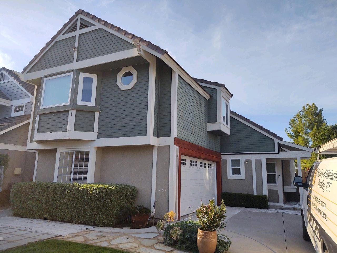 Two-story house with green siding, white trim, a red garage door frame, and a blue sky.