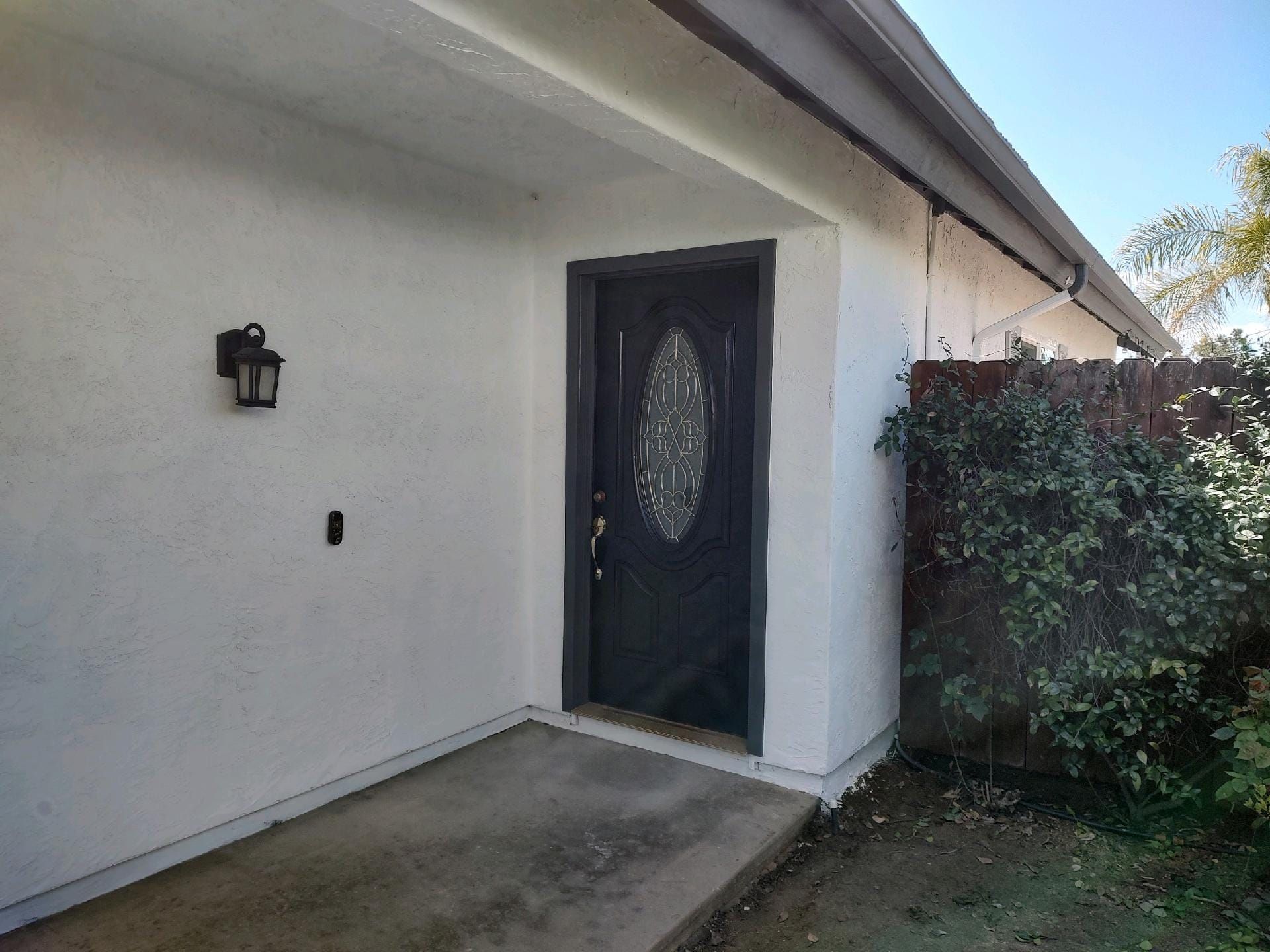 Front door of a white stucco house with a black door and a small porch. A lantern is on the wall.