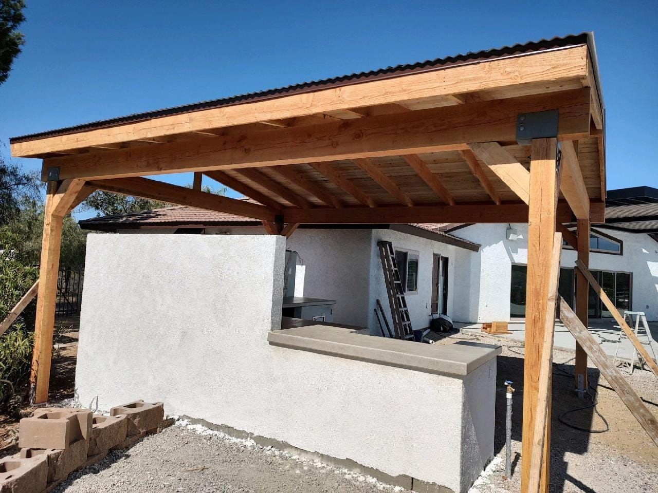 Wooden structure with stucco wall, counter, and corrugated roof under construction outdoors.