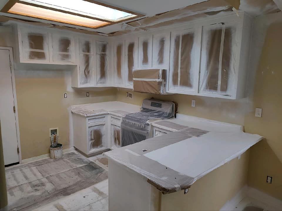 Kitchen being painted; cabinets and countertops covered in plastic; white paint.