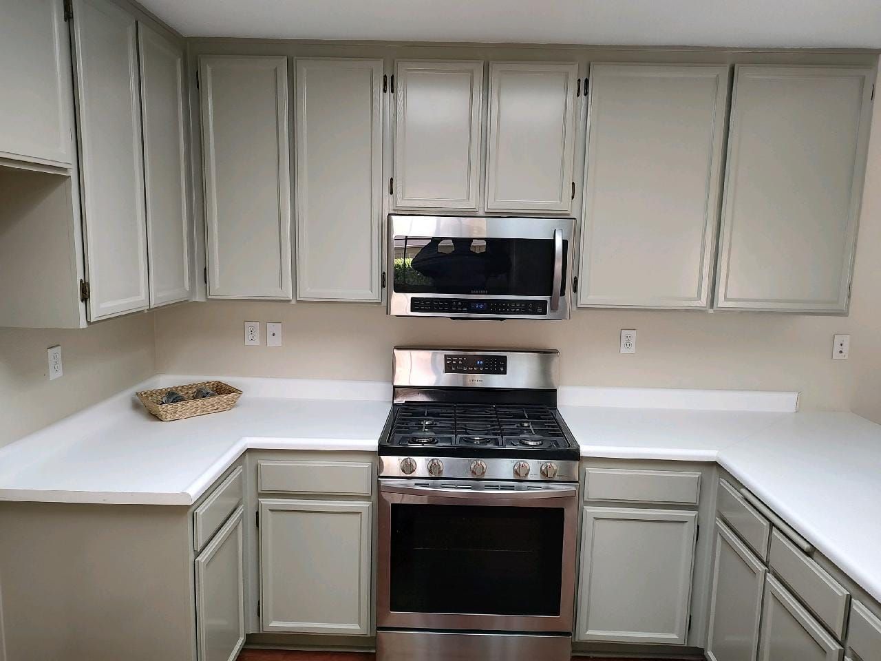 Kitchen with light grey cabinets, stainless steel appliances, and white countertops.