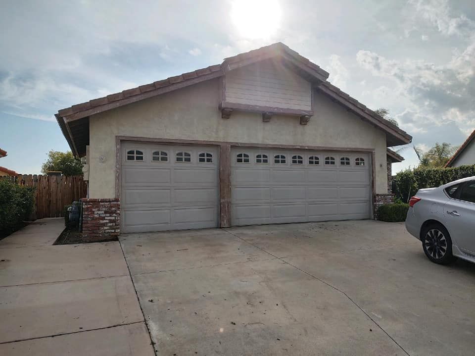 Two-car garage with light gray doors, beige stucco walls, and a car parked in driveway on a sunny day.