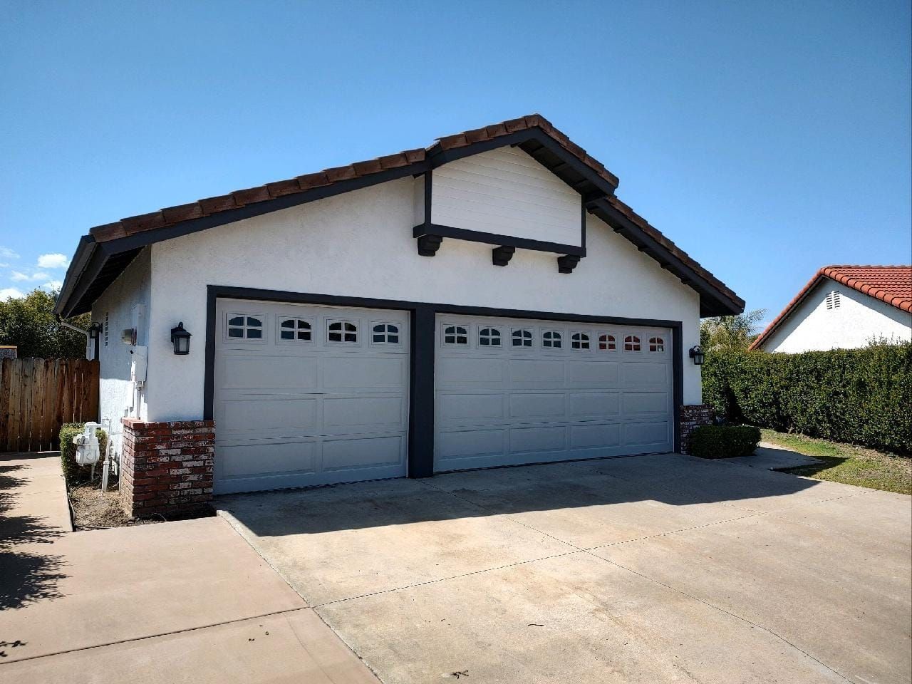 Two-car garage with grey doors, white stucco exterior, and red tile roof under a clear blue sky.