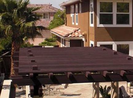 Brown pergola over a patio, with a two-story brown house in the background. Palm tree visible.