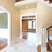 Entryway with beige walls, tiled floor, doorway leading to room with window and wooden staircase.