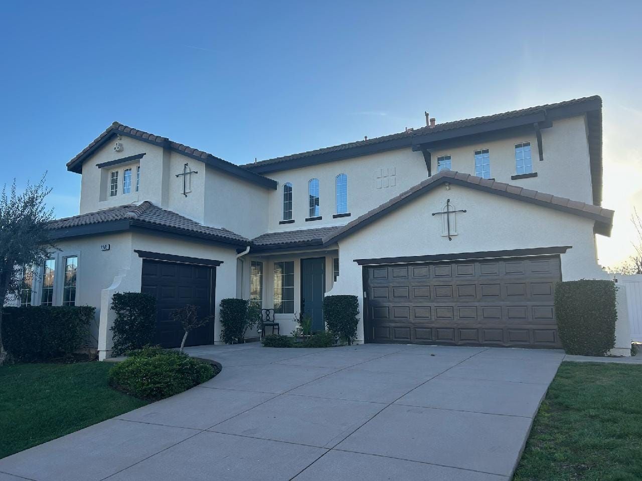 Two-story beige house with brown garage doors and driveway, blue sky.