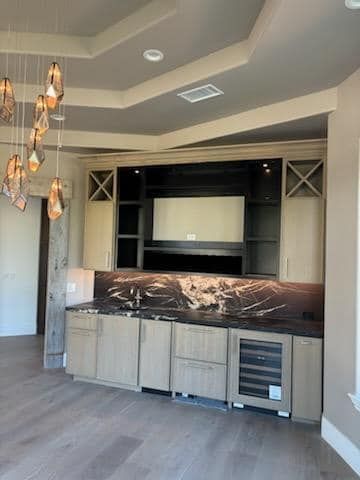 A built-in bar area with gray cabinets, dark countertop, a wine fridge, and a large screen in a light-colored room.