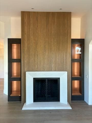 Fireplace with wood paneling, white mantel, and copper-lined bookshelves, in a light-colored room.
