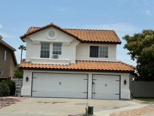 Two-story white house with orange tile roof, two-car garage, windows, and blue sky.