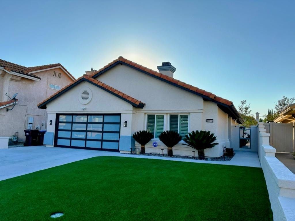 House exterior with modern glass garage door, green lawn, and stucco walls.