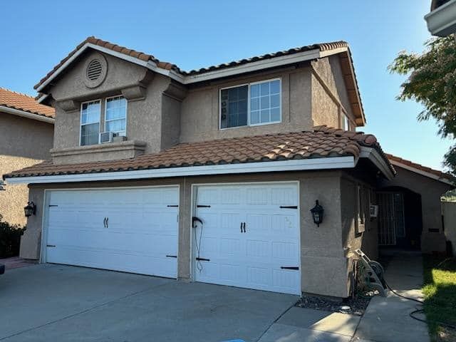 Two-story beige house with a red-tiled roof and two-car garage. Blue sky overhead.