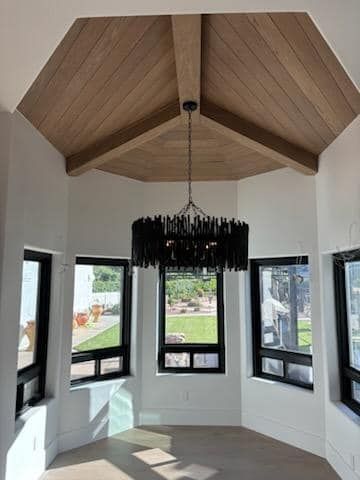 Bright, open room with a light wood-paneled ceiling, black chandelier, and windows overlooking a yard.