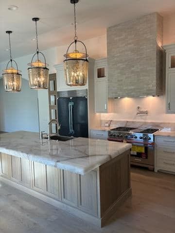 Elegant kitchen with marble island, light wood cabinets, and three pendant lights.