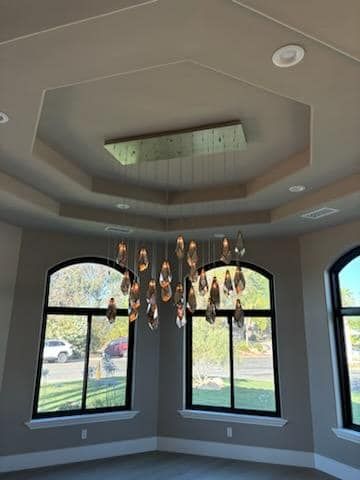 Elegant chandelier with teardrop crystals hangs from a multi-tiered, octagonal ceiling above arched windows.