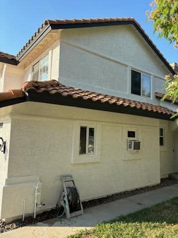 Two-story stucco building with a red tile roof and multiple windows. A ladder and hose are in front.