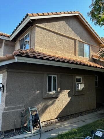 Two-story stucco home with tile roof, windows, and an air conditioning unit on a sunny day.