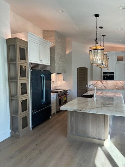 Modern kitchen with marble countertops, island, pendant lights, and dark refrigerator.