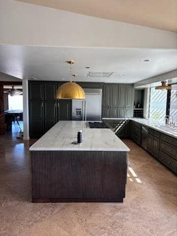 Modern kitchen with dark green cabinets, a large island, and a gold pendant light.