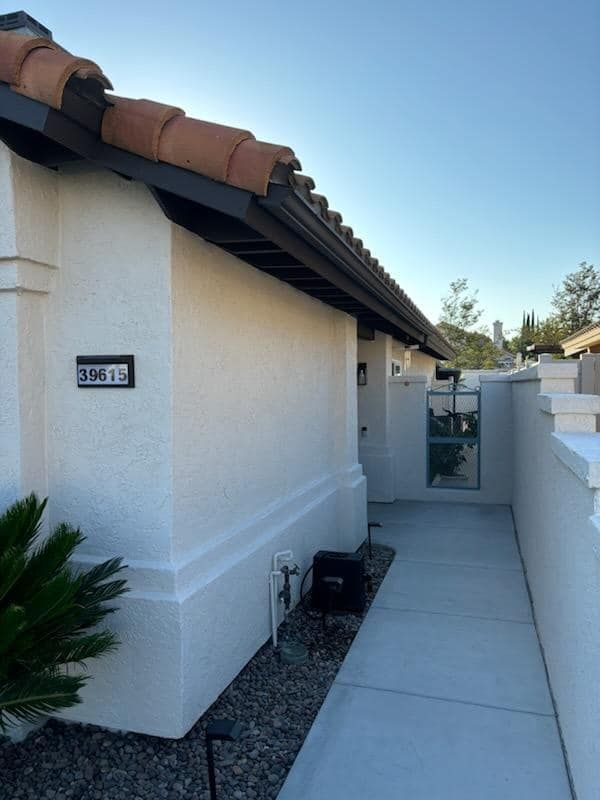 Exterior of a white stucco building with address sign, terracotta roof, and a walkway with gate.