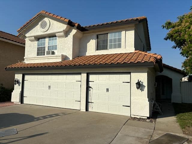 Two-story stucco house with tile roof, two-car garage, and decorative black hardware.