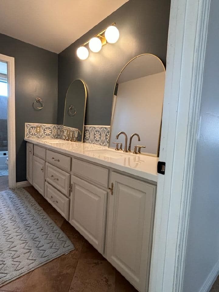 Bathroom with blue wall, white vanity, arched mirrors, and gold light fixture.