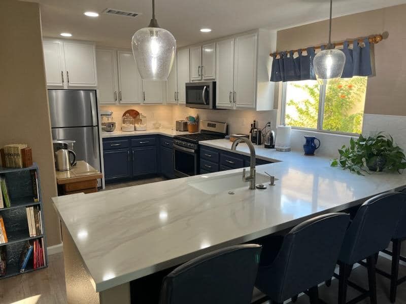 Modern kitchen with white and navy blue cabinets, stainless steel appliances, and a large island with bar stools.