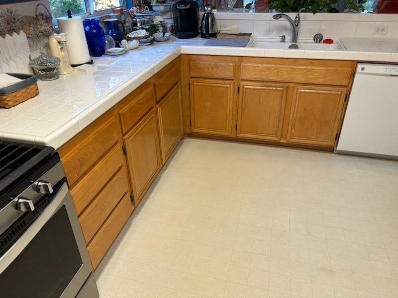 A kitchen with light-colored wood cabinets, white countertops, a stove, and a dishwasher.