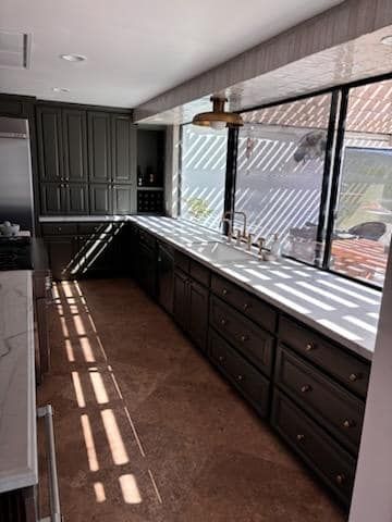 Dark kitchen with cabinets, long countertop, large window, and brown flooring.